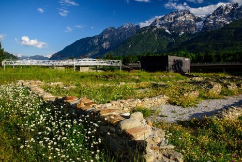 Restored roman walls surrounded by vegetation, with mountains in the distance