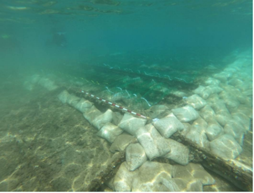 An underwater archaeological site covered by a metal grid structure and surrounded by sandbags