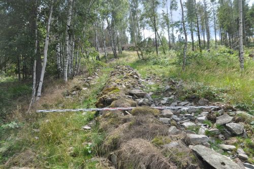 Scattered stones representing the remnants of a clearance cairn, with a marker laid over the stones to indicate the direction of driving that has caused the erosion of the cairn.