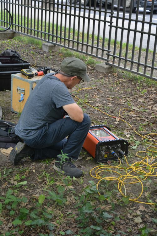 a man crouching next to scientific equipment in a leafy garden