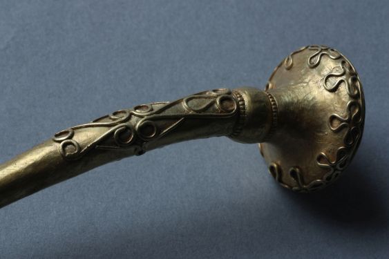 Colour photograph of torc against a grey background showing filigree work